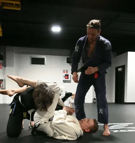 Youth jiu jitsu practitioners spar on the mat under the watchful eye of their coach