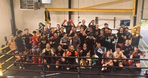 A large group of fighters poses together in a training gym, showcasing team spirit