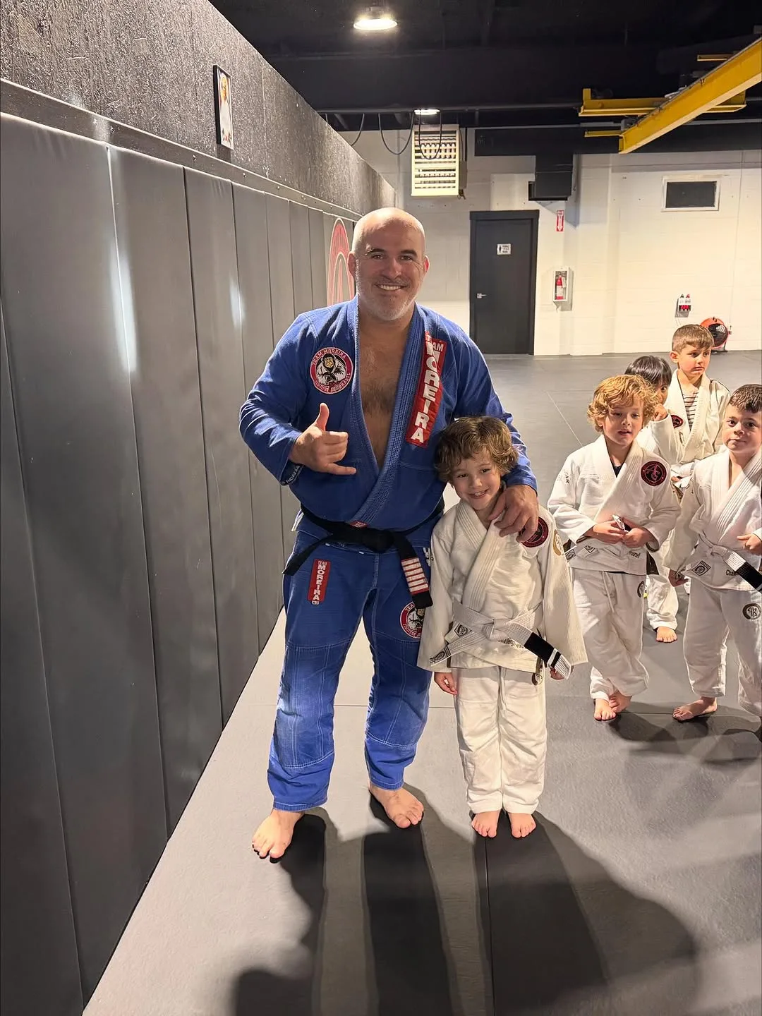 A smiling instructor poses with a young student, while other children wait in line