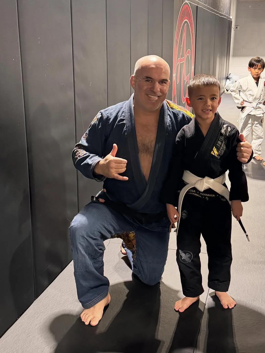 Kids jiu jitsu practice with a smiling adult and a young child in martial arts uniforms