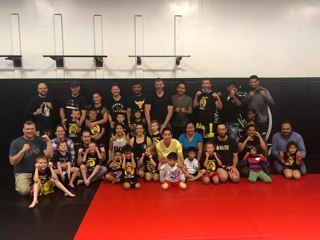 A diverse group of individuals poses together on a wrestling mat, showcasing camaraderie