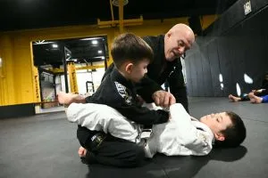 Kids jiu jitsu students practice grappling techniques with an instructor in a dojo