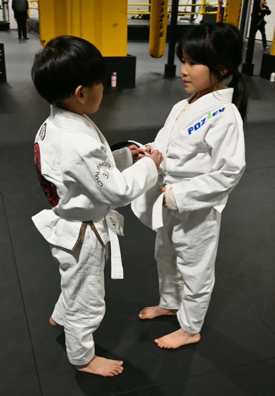 Kids jiu jitsu practitioners tie each other's belts in white uniforms