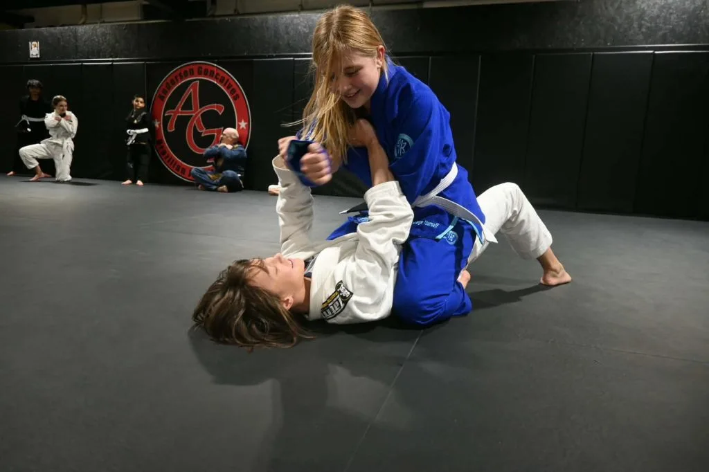 Kids jiu jitsu practitioners grapple on a colorful training mat during practice