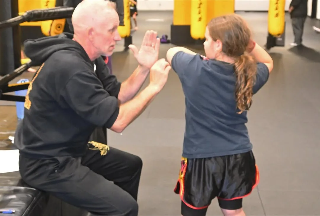 Youth muay thai training session with a coach demonstrating techniques to a young athlete